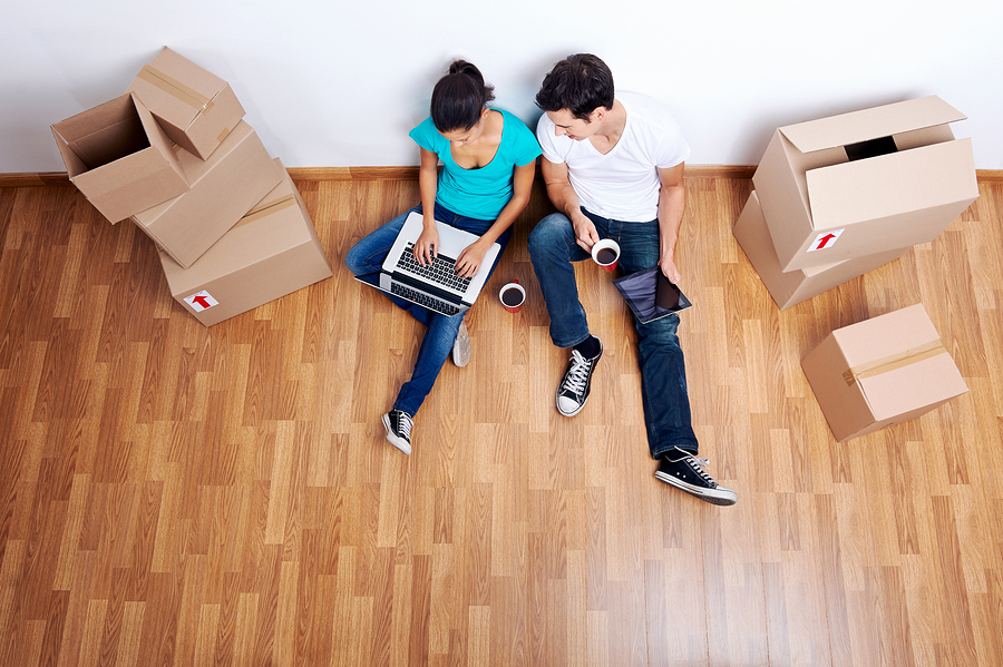 Couple sitting on floor with laptop surrounded by boxes